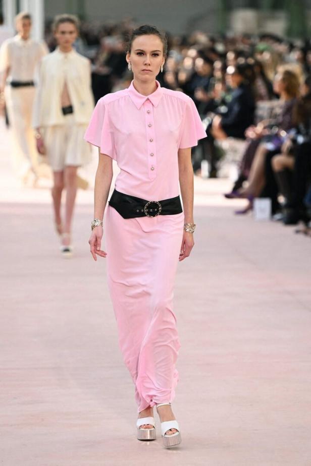 Eine Frau in einem rosa Kleid mit schwarzem Gürtel läuft auf einem Laufsteg.