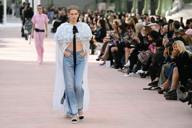 Ein Model läuft auf einem Laufsteg mit einem Cape aus Federn und Jeans mit Strassapplikationen.