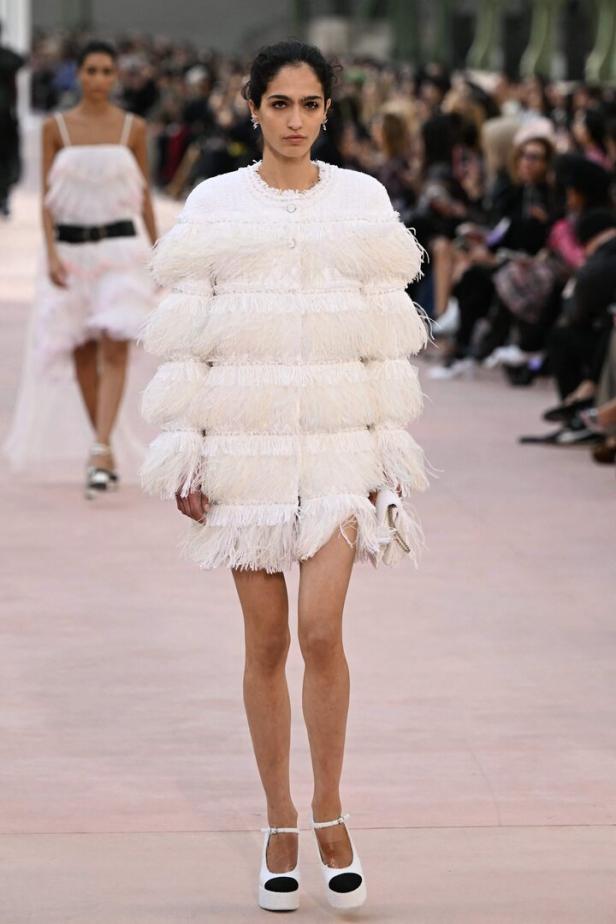 Eine Frau auf dem Laufsteg, die ein weißes, mehrlagiges Fransenkleid trägt.