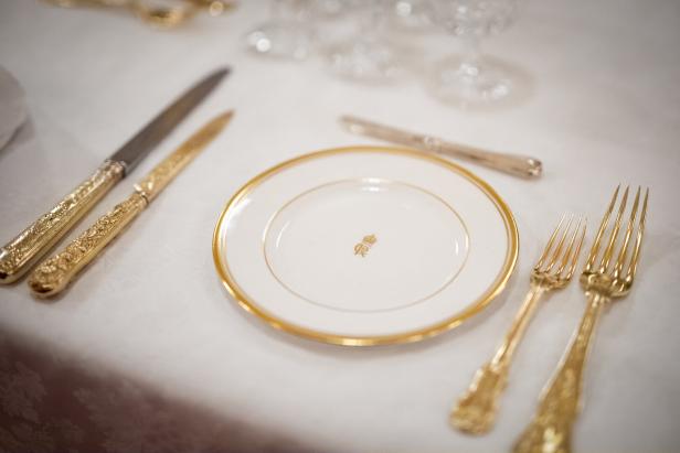 Ein gedeckter Tisch mit goldenem Besteck und einem Teller mit königlichem Monogramm.