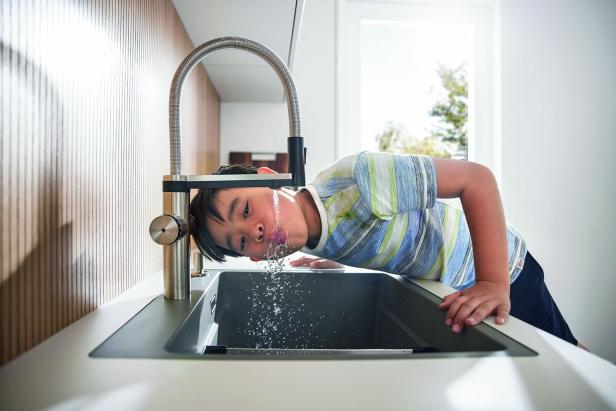 Ein Junge trinkt Wasser direkt aus einem modernen Wasserhahn in der Küche.