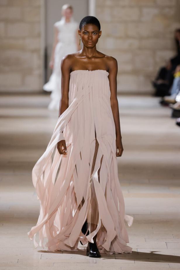 Eine Frau präsentiert ein trägerloses, hellrosa Kleid mit Fransen auf einem Laufsteg.