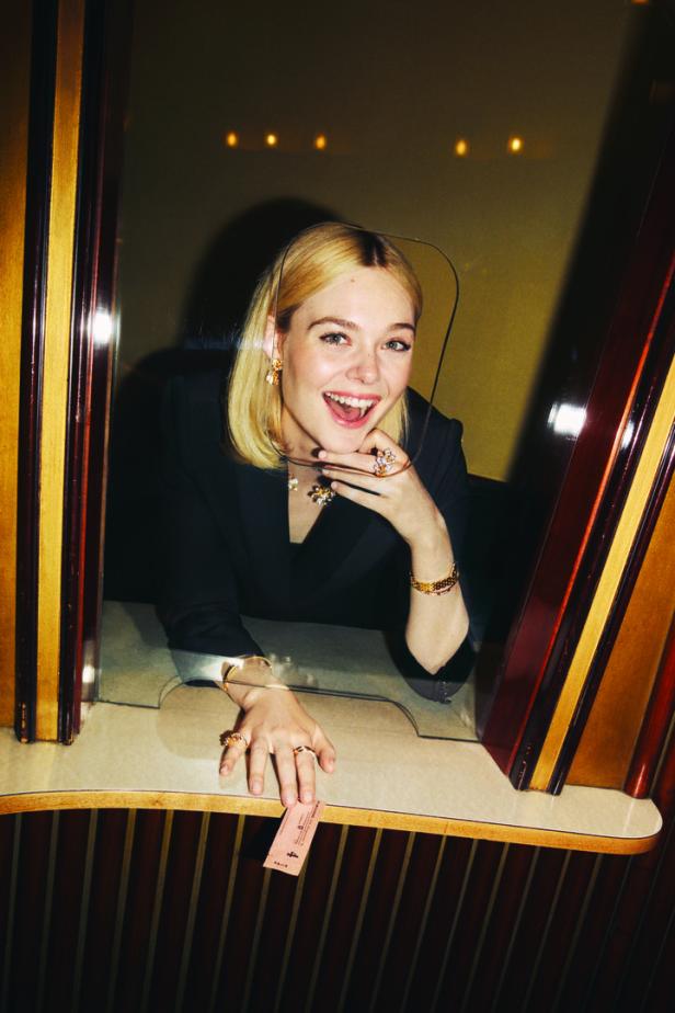 Elle Fanning lächelt an einem Ticketschalter und hält eine Eintrittskarte in der Hand.