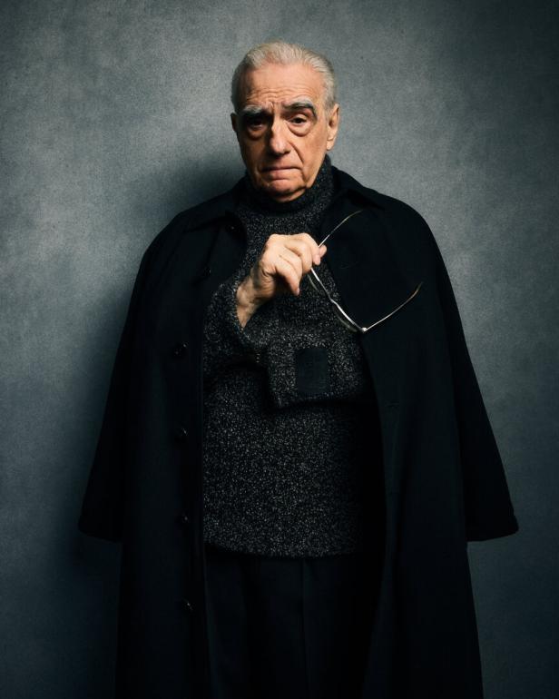 Martin Scorsese hält eine Brille in der Hand und trägt einen schwarzen Mantel.