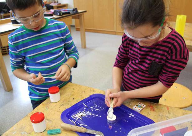 Zwei Kinder mit Schutzbrillen basteln an einem Tisch mit Kerzen und Streichhölzern.
