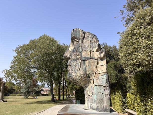 Eine große, beschädigte Steinskulptur eines Kopfes in einem Park.