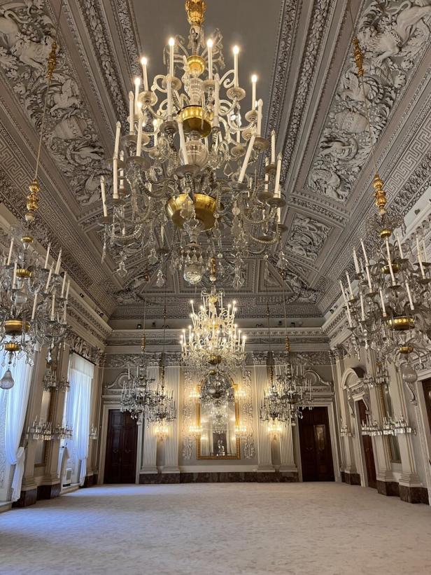 Ein prunkvoller Saal mit mehreren Kristalllüstern und Stuckdecken.