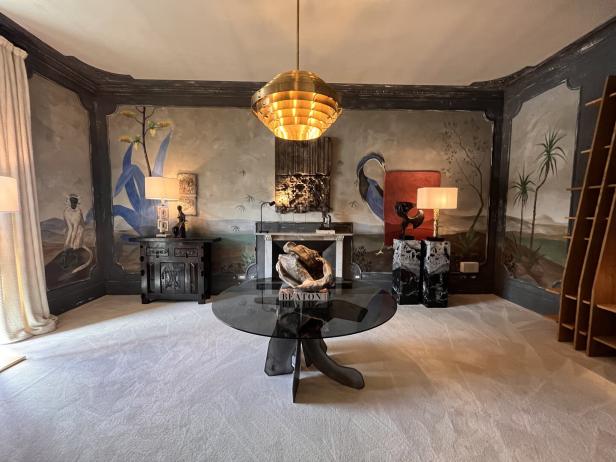 Ein Wohnzimmer mit bemalten Wänden, einem runden Glastisch und einer goldenen Hängelampe.