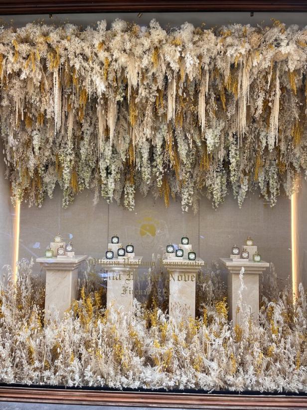 Ein Schaufenster mit Parfümflaschen auf Säulen, umgeben von Trockenblumen.