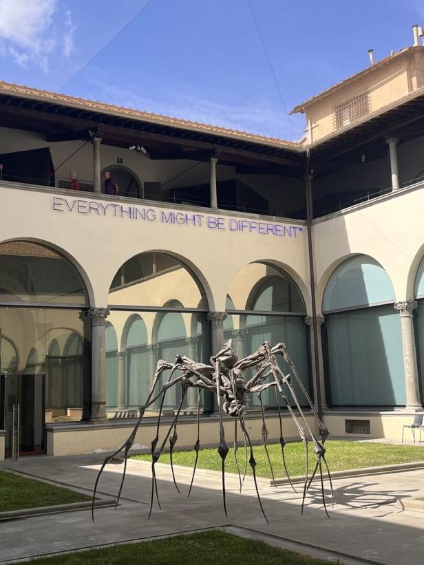 Eine Spinnenskulptur steht im Innenhof eines Gebäudes mit der Aufschrift „Everything might be different“.