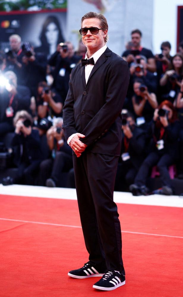 Brad Pitt auf einem roten Teppich, gekleidet in einen Anzug und Adidas-Sneakers.
