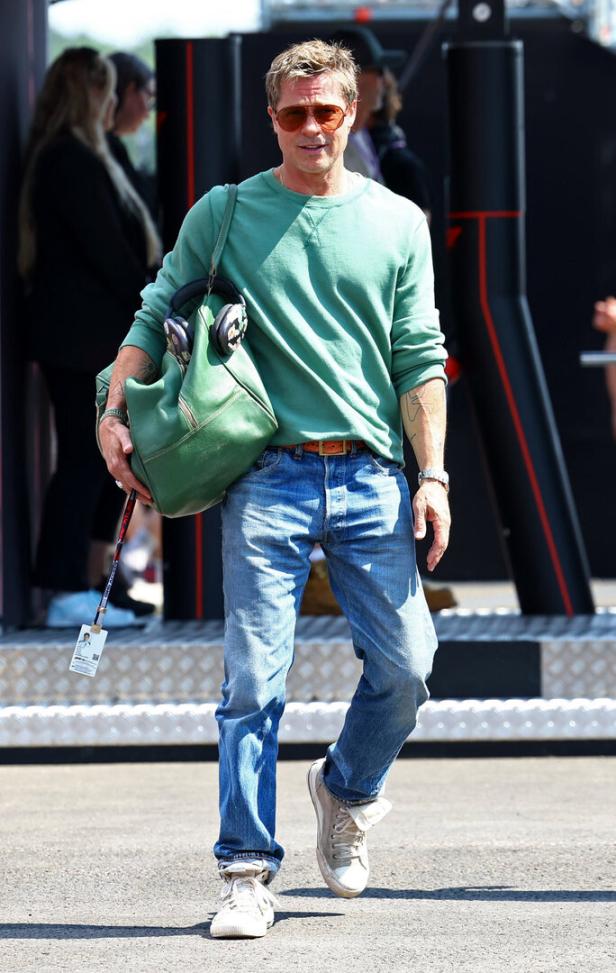 Brad Pitt mit Sonnenbrille, Jeans und grüner Tasche bei einem Formel-1-Rennen.
