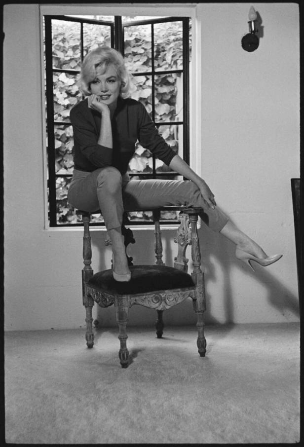 Marilyn Monroe sitzt auf einem Stuhl vor einem Fenster.