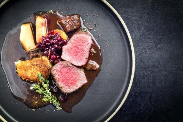 Wildfleisch mit Preiselbeeren, Kartoffelbeilage und Soße auf einem Teller.