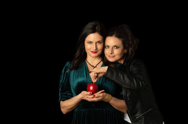 Zwei Frauen posieren mit einem roten Apfel vor einem schwarzen Hintergrund.