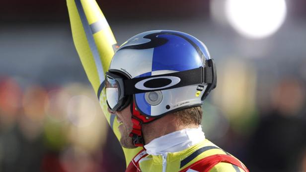 Ein Skirennfahrer mit Helm und Skibrille hebt einen gelben Skiarm.