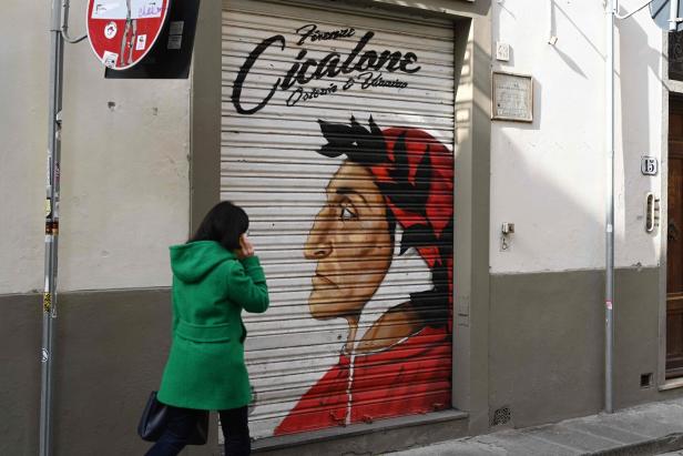 Eine Frau geht an einem Geschäft mit einem Graffiti von Dante Alighieri vorbei.