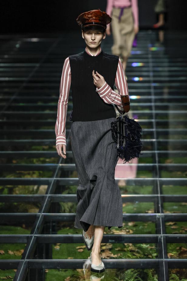 Ein Model mit Hut, Weste und Rock auf einem transparenten Laufsteg.