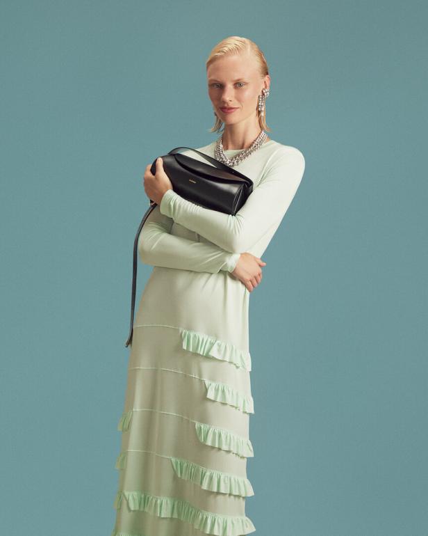 Eine Frau in einem hellgrünen Kleid mit Rüschen hält eine schwarze Handtasche.