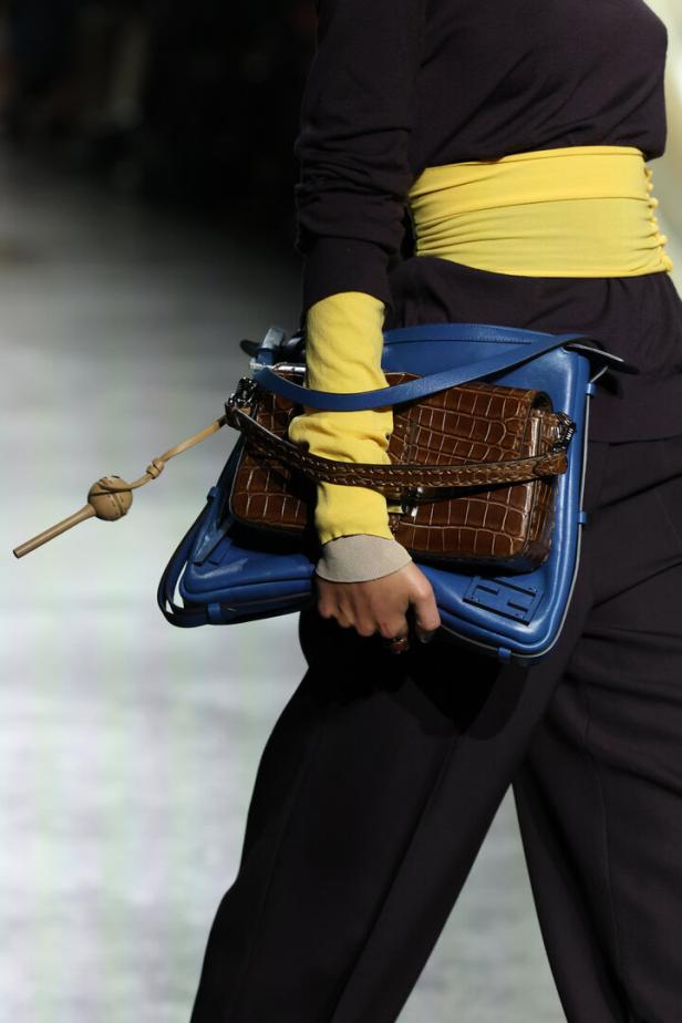 Eine Person trägt eine blaue Handtasche mit einer braunen Tasche aus Krokodilleder darüber.