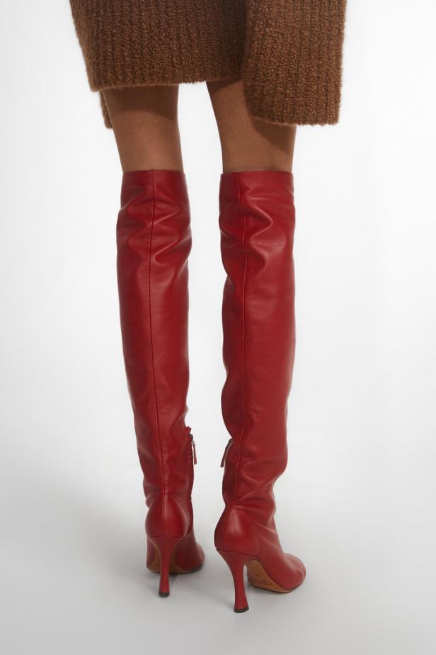 Eine Frau trägt rote Overknee-Stiefel mit Absatz und einen braunen Pullover.