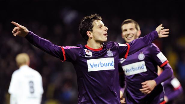 Ein Fußballspieler jubelt mit ausgestreckten Armen und zeigt mit dem Finger nach oben.