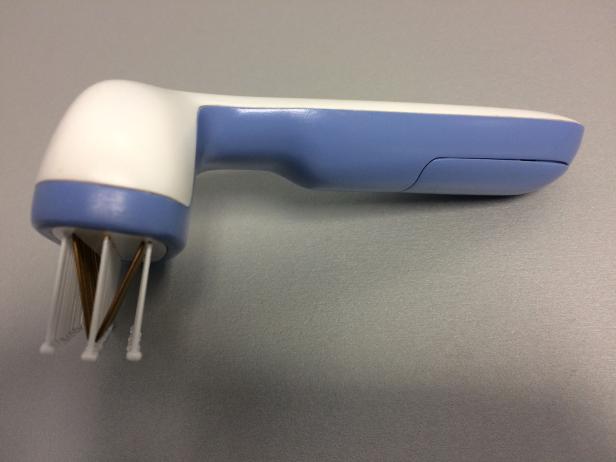 Eine Reinigungsbürste mit blau-weißem Griff und Lamellen steht auf einer grauen Oberfläche.