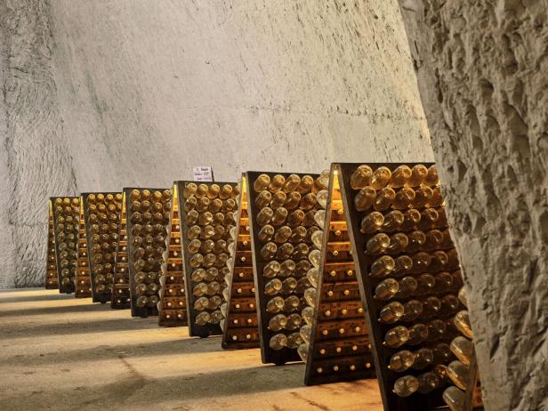 Rüttelpulte, in denen Champagnerfalschen eingeordnet sind, in einem hohen Weinkeller aus Kalkgestein.