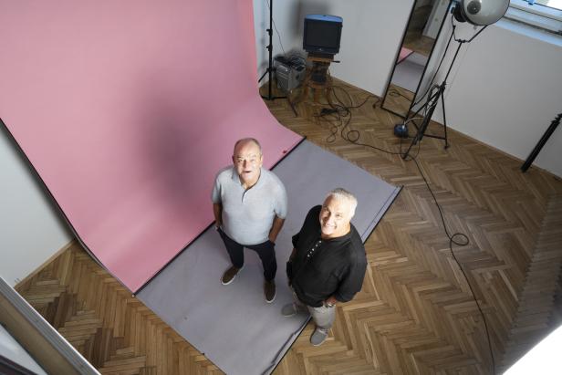 Zwei Männer stehen in einem Fotostudio vor einem rosa Hintergrund.