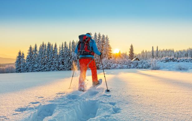 Mann stapft mit Schneeschuhen durch den Tiefschnee, Winterwandern bei Sonnenuntergang