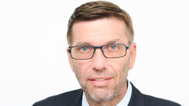 Porträt eines Mannes mit Brille und Anzug vor einem weißen Hintergrund.