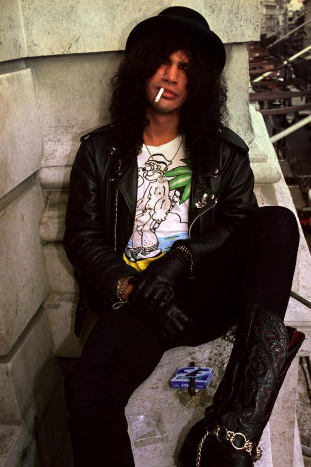 Slash mit Hut, Lederjacke und Zigarette posiert lässig.