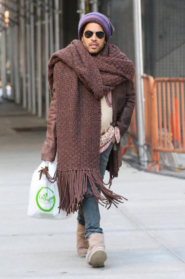 Lenny Kravitz mit Sonnenbrille, Mütze und großem Schal geht die Straße entlang.