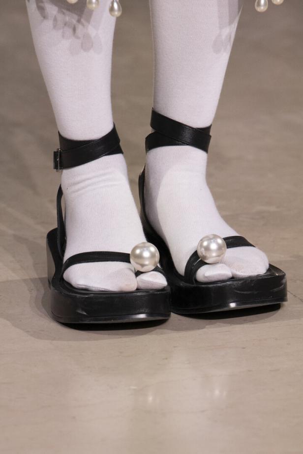 Nahaufnahme von Füßen in weißen Socken und schwarzen Sandalen mit großen Perlen.