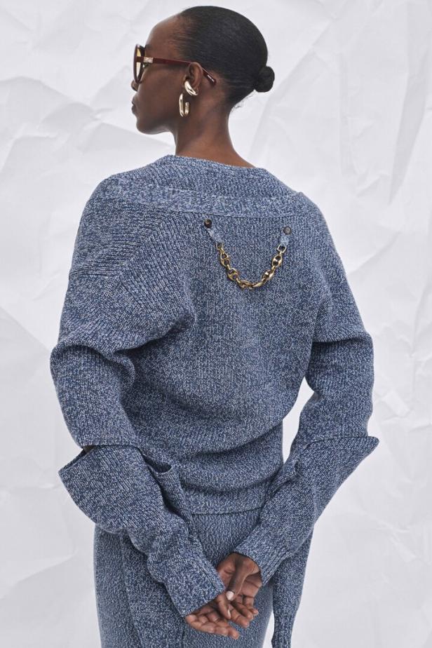 Eine Frau trägt einen blauen Strickpullover mit einer goldenen Kette auf dem Rücken.