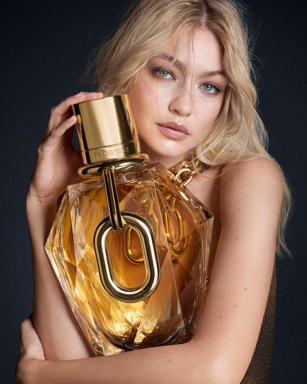 Gigi Hadid umarmt einen großen, goldenen Flakon des Parfüms „Fame“ von Paco Rabanne.
