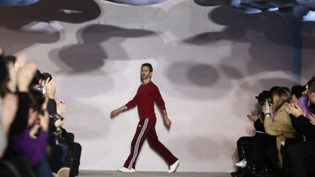 Ein Mann in rotem Trainingsanzug geht auf einem Laufsteg, während das Publikum applaudiert.