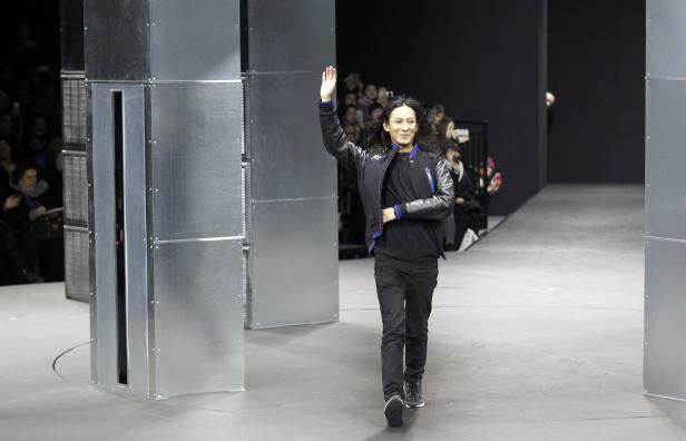 Ein Mann mit dunklen Haaren winkt auf einem Laufsteg.