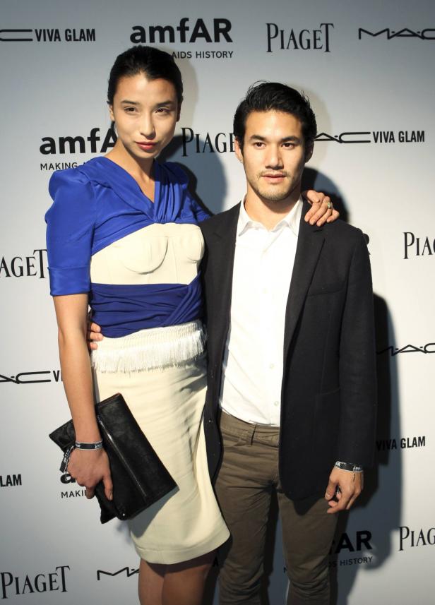 Eine Frau in einem blau-weißen Kleid und ein Mann in einem Anzug posieren vor einer Wand mit Logos.