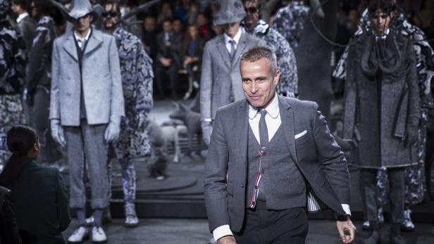 Thom Browne bei einer Modenschau, umgeben von Models in grauen Anzügen.