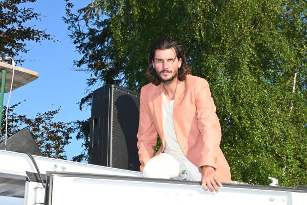 DJ Wolfram mit Sakko sitzt vor einer Box auf einem Container.