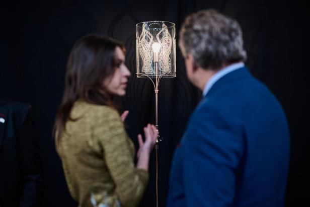 Zwei Personen unterhalten sich vor einer Stehlampe mit einem Lampenschirm aus Glas.