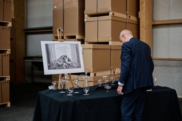 Ein Mann betrachtet eine Ausstellung mit Gläsern und einer Grafik vor einem Lager mit Kartons.