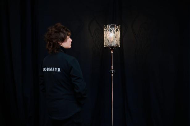 Eine Person betrachtet eine Stehlampe der Marke Lobmeyr vor einem schwarzen Hintergrund.