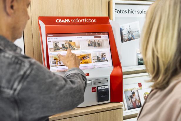 Ein Mann zeigt einer Frau den CEWE-Sofortfotos-Automaten