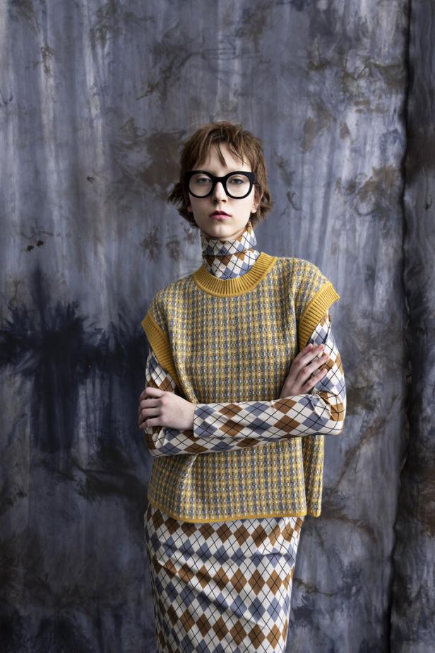 Eine Frau mit Brille trägt ein gelbes Oberteil mit Rautenmuster und einen passenden Rock.