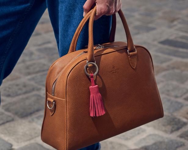 Eine Person trägt eine braune Ledertasche mit einem rosa Quastenanhänger.