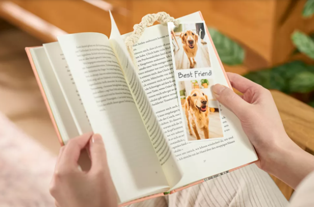 Eine Frau hält ein Buch in den Händen. Auf ihrem Lesezeichen befindet sich ihr Hund.