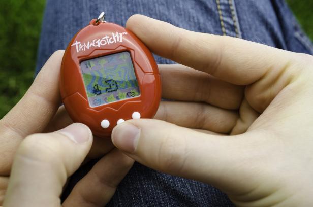 Eine Person hält ein rotes Tamagotchi in der Hand.