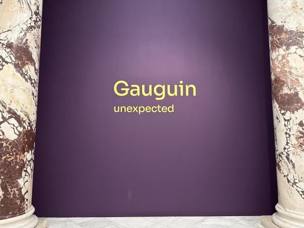 Eine lila Wand, auf der "Gauguin: Unexpected" steht. Links und rechts sind Marmorsäulen.